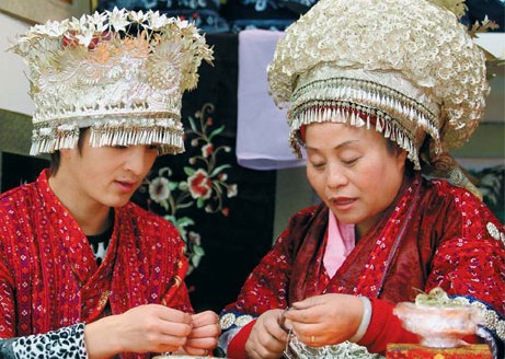 Yang Yufen (right) makes silver crown ornaments at the exhibition. The silver crown she wears weighs 3 kg. Photos by Feng Yongbin / China Daily