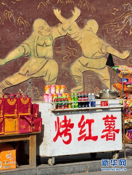 Peddlers cry their wares in front of painted wall of Shaolin Temple.