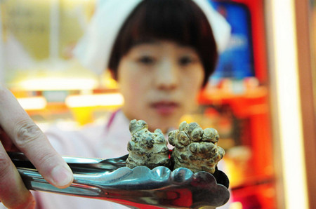 A staff worker shows Yunnan-produced sanqi, a kind of herbal medicine, in a pharmacy in Qingdao, Shandong province. The drought in Yunnan province has resulted in a TCM price hike. [Yu Fangping / for China Daily]