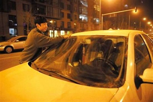 A man cleans his car covered by dusts in Beijing at 11 p.m. on March 30, 2012. [Beijing News/ Han Meng and Wang Jianing]