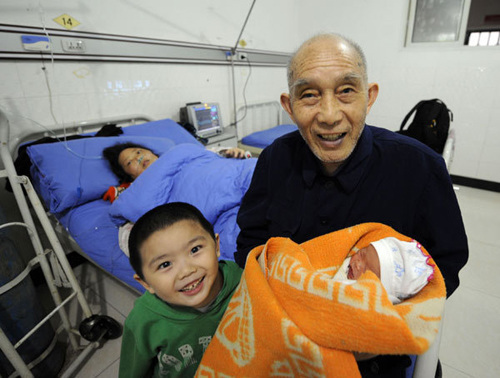 A 75-year-old father, who only gave his surname as Shi, holds his newborn daughter with his son, aged 3, while his wife, 42, lies in bed at a hospital in Chongqing on Tuesday. The infant is the couple's third child and the man's fourth. His first child, a daughter, is 57 years old, and her mother died before Shi remarried. [Photo: Ran Wen /  China Daily]