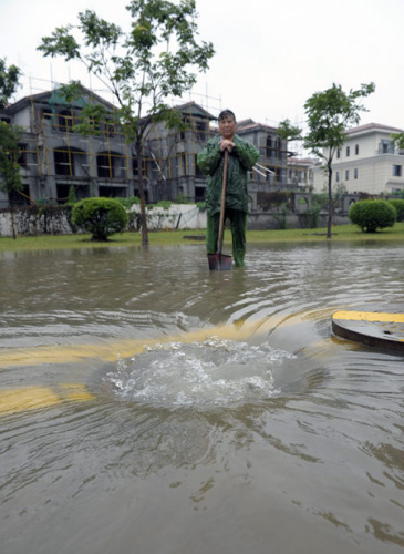 A worker removes a manhole cover to accelerate drainage on a waterlogged road in Nanjing, Jiangsu province, on Thursday. The city experienced heavy rain when it was hit by Typhoon Haikui. 