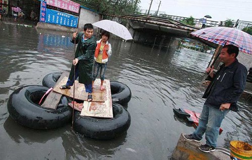 A motor-repair store employee (left) ferries a woman on his self-made raft across a fl ooded crossroad in Beijing's Fengtai district on Sunday after a heavy rain hit the city. [Photo/China Daily]