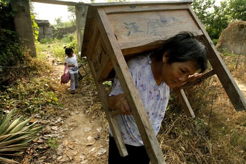 The grandmother of Wang Ziqi, a primary school student, carries a table on Saturday, while his sister carries his schoolbag and a stool on the way to school in Shunhe township. Photo by Wang Zheng / ChangJiang Times