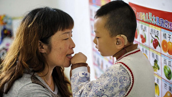 Zhang Tielian helps a hearing-impaired boy to feel the vibration of air during a pronunciation training class in Xiaoxia Hearing-impaired Child Care Center in Hohhot, North China's Inner Mongolia, Oct 13, 2012. [Photo/Xinhua]