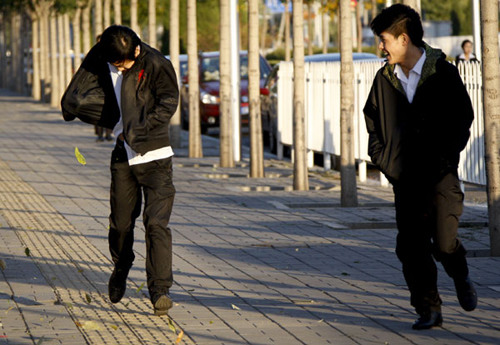 Two young men struggle to walk in strong winds in Chaoyang district, Beijing, on Tuesday. Kuang Linhua / China Daily