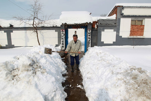 A resident in Beijing's Yanqing county clears snow in front of his house on Monday. The biggest snowfall the county has seen in 52 years caused power outages in 57 villages, brought down thousands of trees and killed numerous livestock. Cui Meng / China Daily