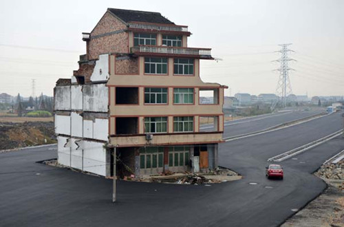 Part of a residential building stands in the middle of a road yet to be officially used in Wenling, Zhejiang province, on Thursday. Its residents have failed to reach an agreement with the government over compensation they should receive for the building's demolition. Jin Yunguo / for China Daily 