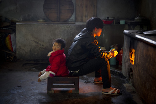 Shi Rutong (left), 3, and Da Di, who are both orphans, warm themselves by a stove in the kitchen of Zifeng Temple in Jieyang, Guangdong province, on Saturday. [Sun Junbin/For China Daily]