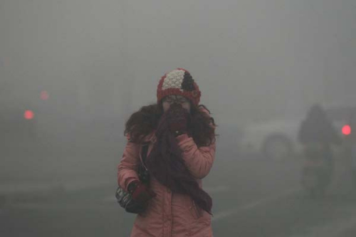 A woman covers her nose when walking through dense fog caused by heavy pollution in Beijing on Tuesday. [Bai Jikai / for China Daily] 