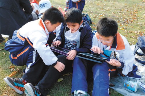 Two primary school students playing games on their iPads while another keenly watches. Electronic games and devices, including iPads and smartphones, are making up an increasingly large share of the Chinese toy market. Traditional children's presents such as dolls and toy cars have been hit hard. Zhu Haiwei / For China Daily