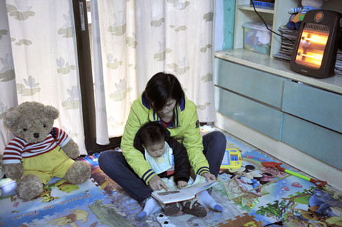 A mother reads a story to her child in front of an electric fi re in Fuzhou, Fujian province, on Friday. LIU TAO / FOR CHINA DAILY