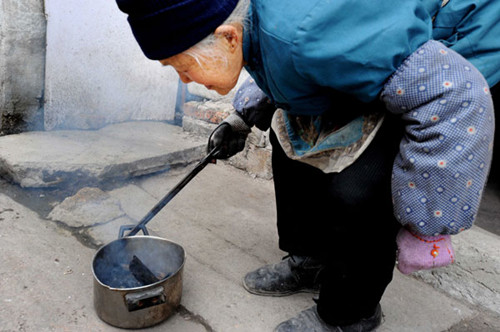 An elderly woman stokes a fire to keep warm in Guiyang, Guizhou province, on Jan 13. WU DONGJUN / FOR CHINA DAILY 