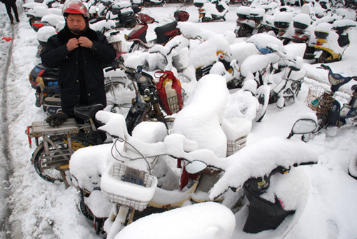 A man parks an electric motor car in Zhenjiang, Jiangsu province, on Tuesday. A snowstorm hit the province on Monday and continued through Tuesday, prompting the local meteorological bureau to issue a blue alert for the winter weather. [LI ZHONG / FOR CHINA DAILY]