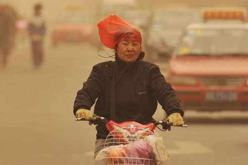 A plastic bag protects a cyclist's head as she braves a sandstorm in Taiyuan, Shanxi province. [Liu Jiang / China Daily]