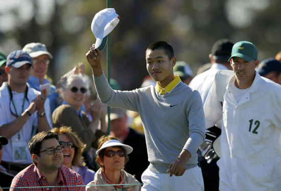 Amateur Guan Tianlang of China tips his hat to the crowd as he walks onto the first tee with caddie Brian Tam (R) during third round play in the 2013 Masters golf tournament at the Augusta National Golf Club in Augusta, Georgia, April 13, 2013. [Photo/Agencies]