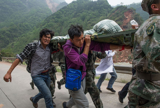 Volunteers Yang Chengcheng (left) and Xiao Long, from Southwest University for Nationalities in Chengdu, join soldiers to rush injured people to an aid center 10 kilometers away in Lushan, Sichuan province, on Sunday.  [Photo/Xinhua]