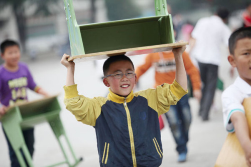 Primary students in Ya'an city, Sichuan province, return to school for the first time on Thursday since an earthquake hit the area on April 20. Their school was badly damaged during the quake and they now attend classes in prefabricated houses. Photo by Zhang Xiaoli / For China Daily