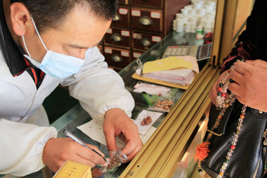 Pharmacist Tenzin writes the name of a traditionally made Tibetan drug on a tag for patients. Wang Huazhong / China Daily