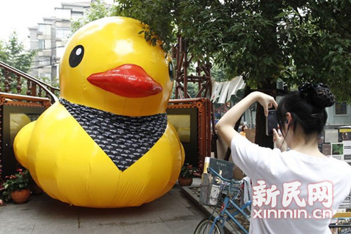 A scaled replica of the Rubber Duck by Dutch conceptual artist Florentijn Hofman is seen along a street next to a vendor waiting for customers in Shanghai, June 13, 2013. [Photo: Xinmin.cn]