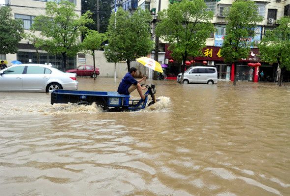 A man wades through rain water on a tricycle in Nanchang, capital city of East China's Jiangxi province, June 28, 2013. [Photo/Xiong Jiafu/Asianewsphoto]