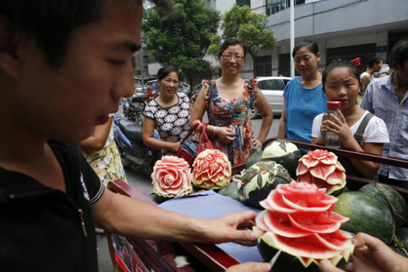 Zhang Yunxiao carves a watermelon in Xiangyang, July 22, 2013. Zhang, a watermelon seller in Xiangyang, Central China's Hubei province, carved flowers onto a watermelon. Prices for the carved watermelons range from 20 yuan ($3.26) to 50 yuan. [Photo/Asianewsphoto]