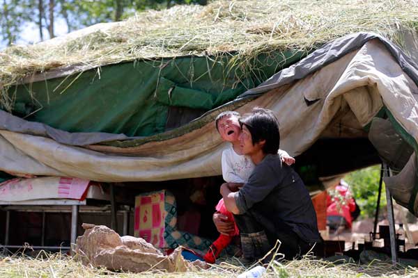 Three-year-old Wang Xiru cries in the arms of her father on Tuesday in Lalu, Gansu province. They have to live in a tent after their house collapsed in the earthquake. photo by Feng Yongbin / China Daily