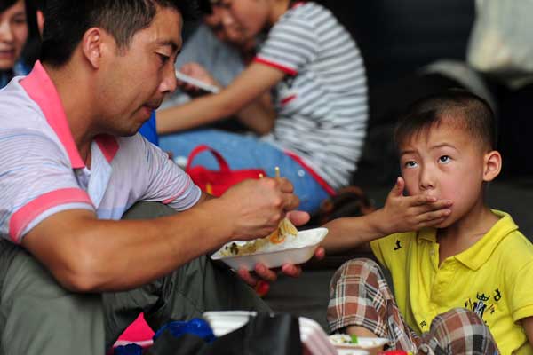 A migrant father feeds his son while waiting for the train at Hefei railway station in Anhui province. Roughly 15,000 migrant parents have taken part in the Maple Women's Psychological Counseling Center's free program to learn the best way to teach their children.Photo provided to China Daily