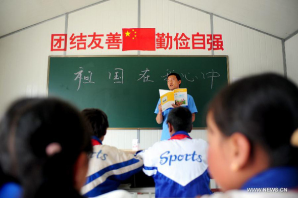 A teacher introduces new textbooks to students in a prefab classroom in the Zhazha Primary School in Yongxing Village, Minxian County of northwest China's Gansu Province, Aug. 25, 2013. Altogether 230 schools damaged in the earthquake in Minxian County started to roll in students on Sunday, and the new term would start on Aug. 26. A 6.6-magnitude earthquake jolted juncture area of Minxian and Zhangxian counties on July 22, in which 230 schools in Minxian were damaged to different extent. (Xinhua/Zhang Meng) 