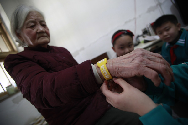 Pupils in Jinan, capital of Shandong province, help a senior resident wear a yellow wrist band in March, 2013. The band, specially designed for Alzheimer's patients, contains the information of senior residents and enables them to contact family members in case they get lost. Zheng Tao / for China Daily 