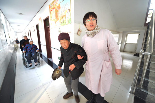 Jin Yonglian, an employee at a nursing home in Zouping, Shandong province, helps an Alzheimer's disease patient back to her room on Jan 9. Dong Naide / for China Daily 