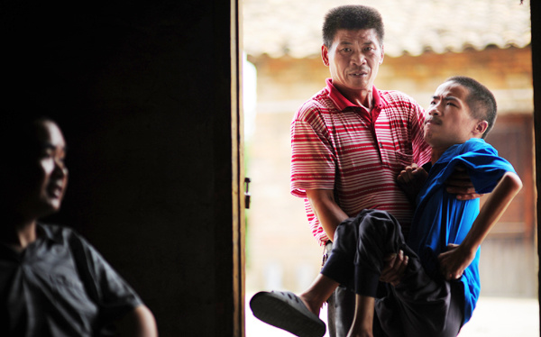 Liu Yuliang, a patient with amyotrophic lateral sclerosis, also known as Lou Gehrig's disease, is helped by his father as he enters his home in Ganzhou, Jiangxi province, on Wednesday. Chen Dichang / for China Daily 