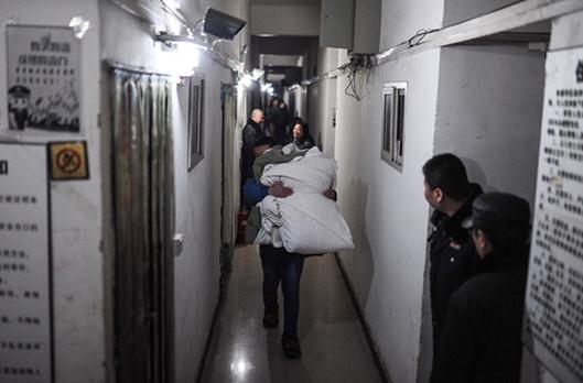 A tenant carries his bedclothes away from a basement room in Beijing's Shijingshan district on Friday. More than 50 migrant families lived in 170 rooms that had been illegally constructed in a basement area the size of a soccer field. Public security, fire protection and administration authorities cleaned up the units.[Wang Yixuan / For China Daily]