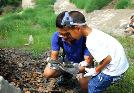 A teacher from Micreate helps a child observe fossilized wood, at Huiyu, a suburban village about 30 km from downtown Beijing that is rich in plant and mammal fossils, in November 2014. [Photo provided to chinadaily.com.cn]