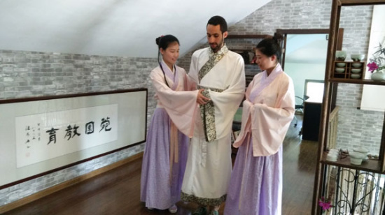 El Amine Cherrat from Ecole Polytechinique, dressed in hanfu, learns the correct way to hold his hands with the help of two students from Nanjing Agricultural University, before practicing how to make tea, on Sunday. Photo provided to chinadaily.com.cn