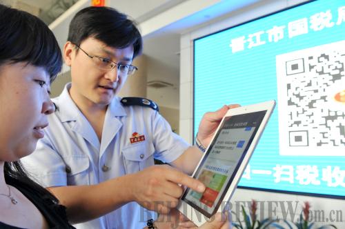 WETAX: Xu Lihui (right), an officer in Jinjiang's State Taxation Bureau helps a company employee access the bureau's public WeChat account, on June 7, 2014 (XU SHANCHUAN)