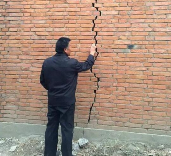 Lu Haisu, a resident of Zhailixi village, Hebei province, examines a crack in the wall of his house. (GUO YARU/XINHUA)