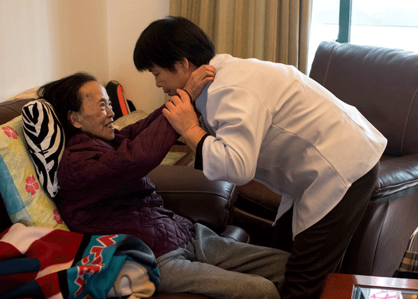 A caregiver employed by Xiaobo Homecare helps an 86-year-old Shanghai resident to sit stably on sofa. The senior's daughter hired the caregiver to assist her mother as she recovers from a stroke. (Photo by Gao Erqiang/China Daily)