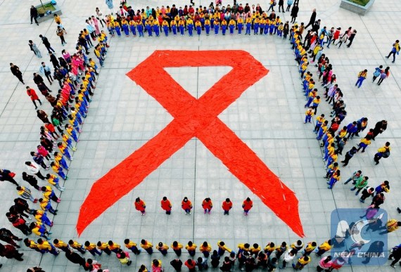 Pupils show a huge red ribbon, the HIV/AIDS awareness symbol, formed by red scarves to mark the World AIDS Day in Dexing City, east China's Jiangxi Province, Dec. 1, 2015.(Photo: Xinhua/Zhuo Zhongwei)