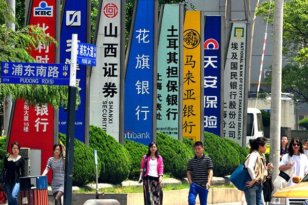 Pedestrians walk past hoards of foreign banks in Shanghai. (Photo/China Daily)