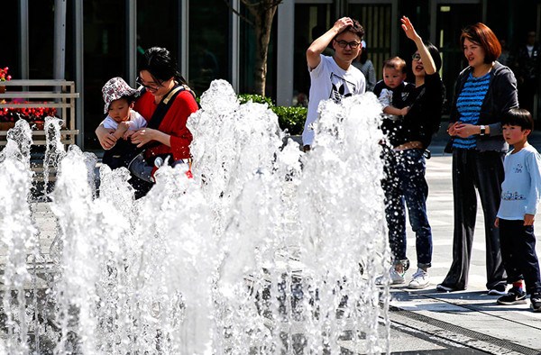 People enjoy a light moment around a fountain on Nanjing West Road in Shanghai on Saturday when the mercury hit 31.2 C. (Yin Liqin/For China Daily)