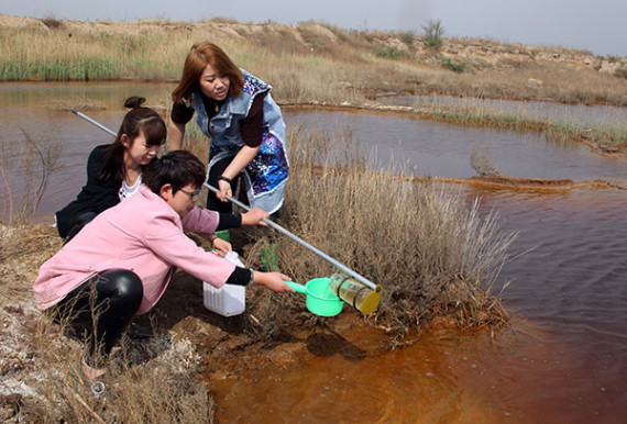 Staff members of the Dacheng county environmental protection bureau's monitoring station collect a water sample on Thursday from a polluted pit in Langfang, Hebei province.(Deng Jia/For China Daily）