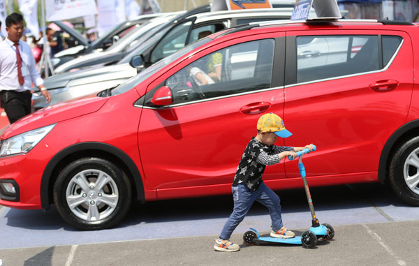 A child riding a scooter passes by a car at an auto exhibition in Beijing. (ZOU HONG / CHINA DAILY)