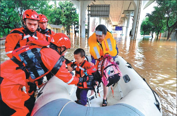 Fire brigade officers escort a student to an elementary school for end-of-semester exams in a raft in the flood-stricken city of Liuzhou, Guangxi Zhuang autonomous region, on Tuesday.Li Hanchi / For China Daily