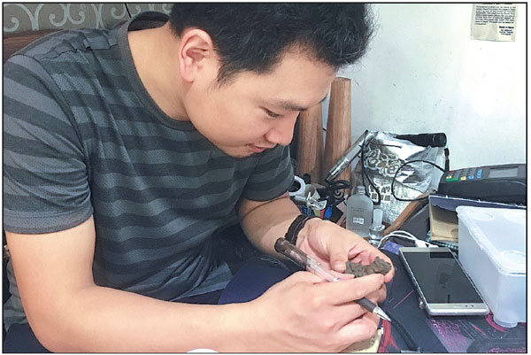 Zhang Neng checks a handicraft item in his swap shop in Guangzhou, Guangdong province. Liang Fengxin/China Daily