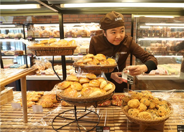 Yang Xiao, 28, who is intellectually disabled, attaches price tags to containers at the bakery.(Photo by Zou Hong/China Daily)