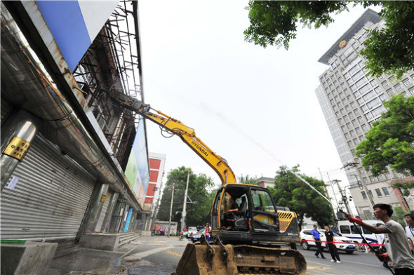 An excavator tears into the Guang'anzhonghai electronics market in Beijing earlier this month as another worker uses a water hose to dampen the dust.  (WANG JIANKANG/FOR CHINA DAILY)