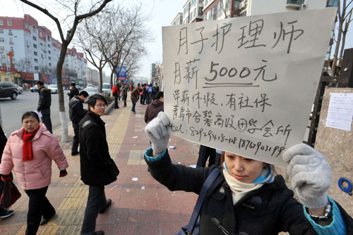 A woman holding a billboard in Qingdao, Shandong province, that states she is looking for confinement nurses with a monthly income of 5,000 yuan ($794) and other remuneration including annual paid leave and social insurance. Zhao Jianpeng / for China Daily 