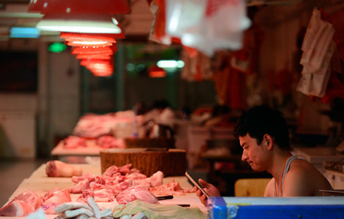 Owner of a pork booth in a food market plays his phone in Chaoyang district, Beijing, July 9, 2015. (Photo: China Daily/Wei Xiaochen)