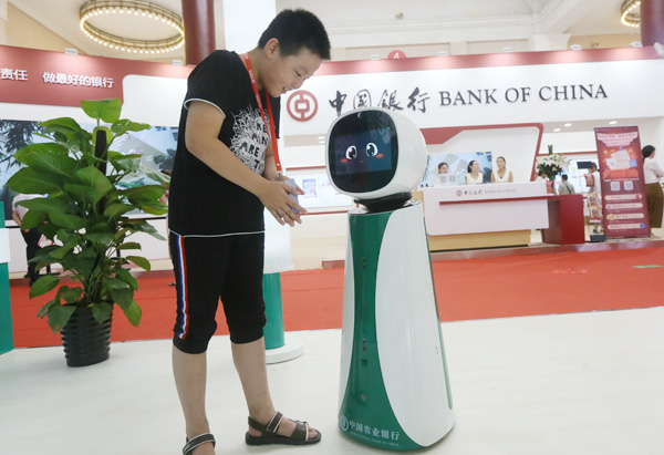 A boy interacts with a robot from Agricultural Bank of China at the 25th China International Finance Exhibition in Beijing on July 28. LEI KESI / FOR CHINA DAILY